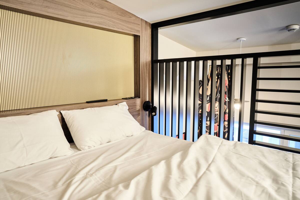 Een moderne slaapkamer met een bed, een houten hoofdbord en uitzicht door een raam met zwarte lijst.