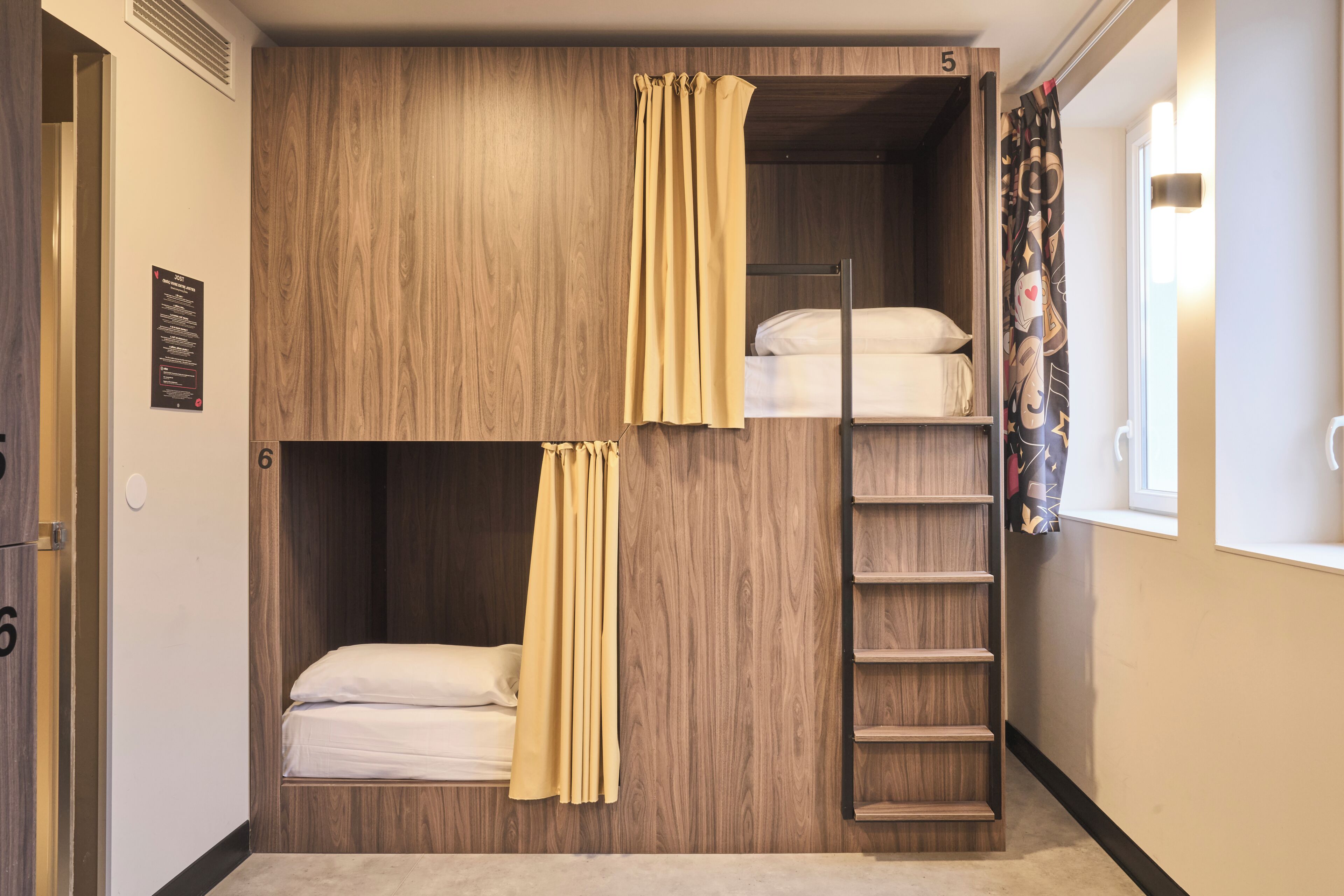 Dormitorio con literas, pared de madera, escalera y ventana con cortinas.