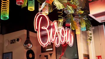 Un letrero de neón con la palabra “Bison” en una tipografía estilizada, rodeado de decoraciones colgantes coloridas y un cuadro en la pared.