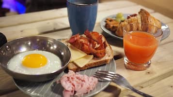 Un plato de desayuno con huevos, tocino, queso, jamón, tostadas y un vaso de jugo de naranja.