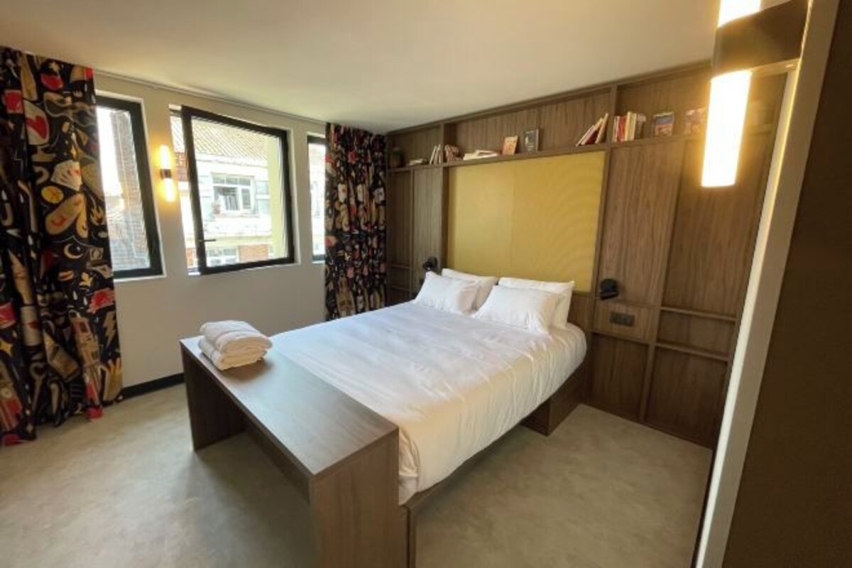 Een hotelkamer met een bed, nachtkastje, gordijnen en een inbouwkast.
