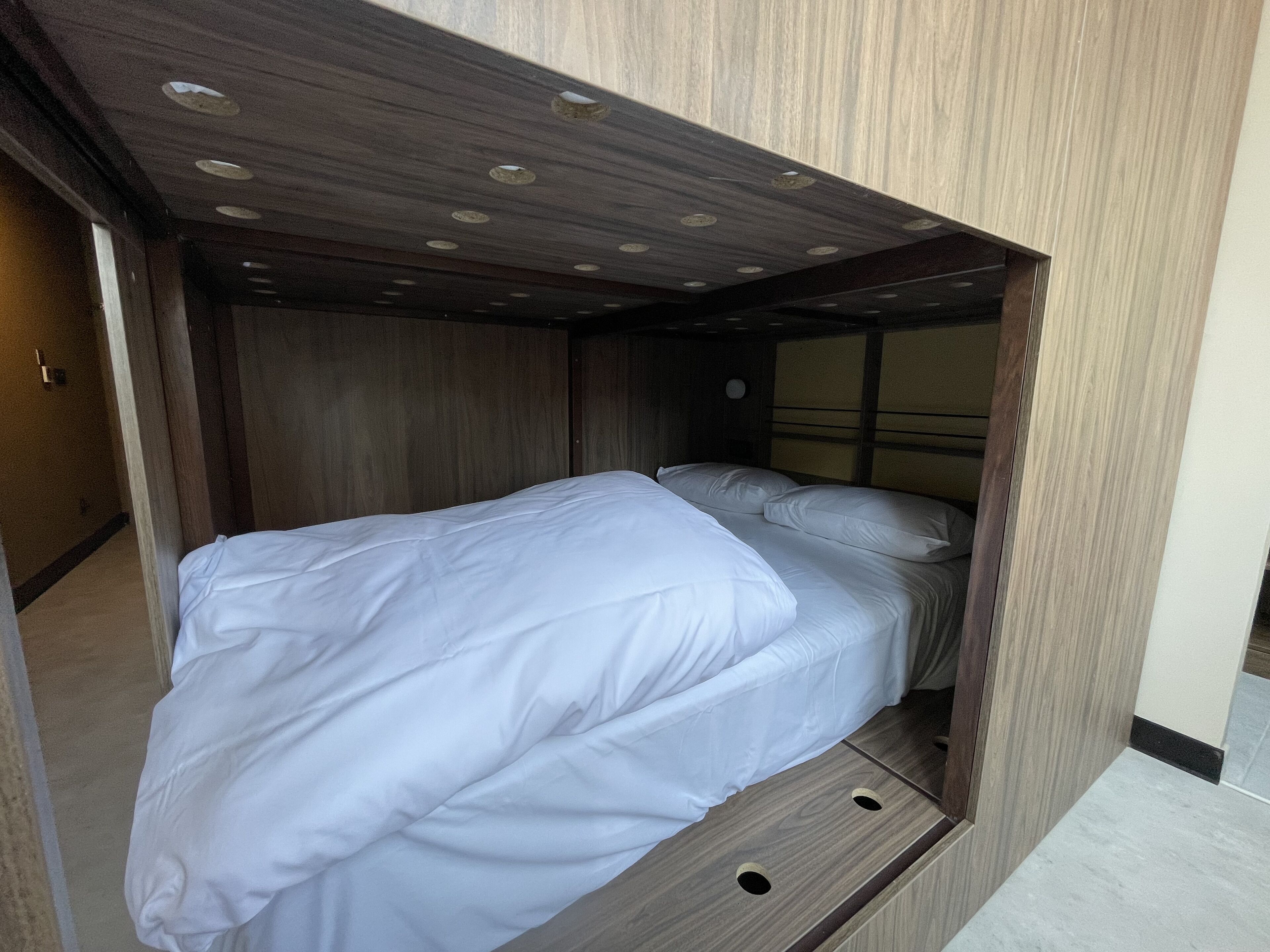 Habitación compacta y moderna con cama integrada, paneles de madera e iluminación empotrada en el techo.