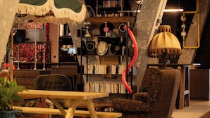 A cozy room with a wooden table, patterned armchair, and a bookshelf filled with books and vinyl records.