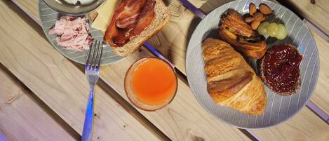 Ein Frühstücksteller mit Eiern, Speck, Käse, Schinken, Toast, Croissants und Marmelade.