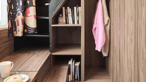 A compact room with a wooden staircase, a small seating area with a table, and a bookshelf.