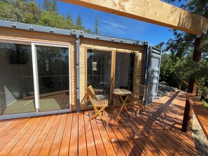 A wooden deck with a glass enclosure, two wooden chairs, and a table.