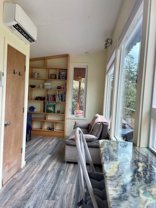 A modern living room with a built-in bookshelf, a sofa, and a large window offering a view of the outdoors.