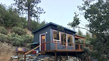 Une cabane dotée d’une terrasse en bois, de fondations en pierre et d’une grande fenêtre.