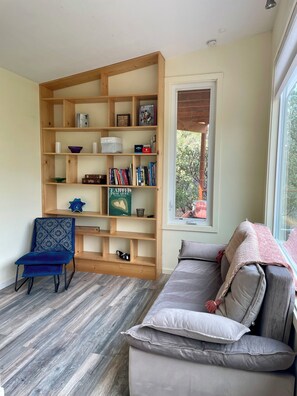 Ein Wohnzimmer mit Bücherregal, einem blauen Sessel, einem grauen Sofa und einem Fenster.