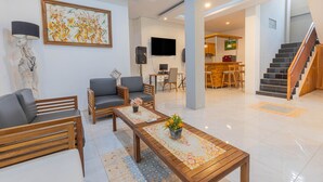 Una sala de estar moderna con un sofá, sillones, una mesa de centro con camino de mesa floral, un cuadro y un televisor.