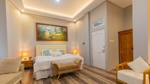 Un dormitorio con una cama, mesitas de noche, un banco, una silla y un cuadro en la pared.