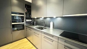 A modern kitchen with built-in appliances, a stainless steel sink, and light-colored cabinetry. - Elegante Unterkunft in Stadtnähe (Adliswil)