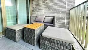 A balcony with wicker furniture, including two chairs and a small table, against a brick wall. - Elegante Unterkunft in Stadtnähe (Adliswil)