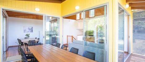 A spacious dining area with a long wooden table and black chairs, large sliding glass doors, and a wooden ceiling.