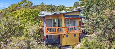 A two-story house with a balcony, surrounded by dense vegetation.