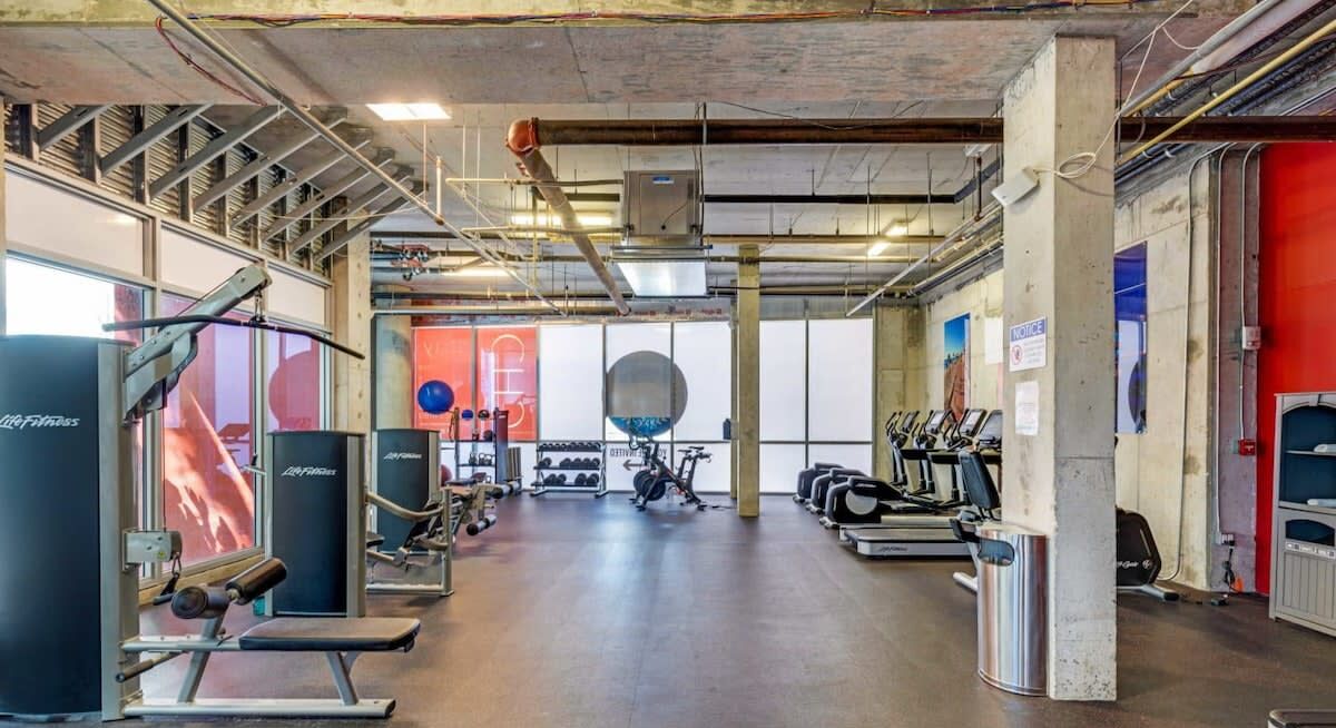 A gym with various exercise equipment, a large mirror, and a red wall.