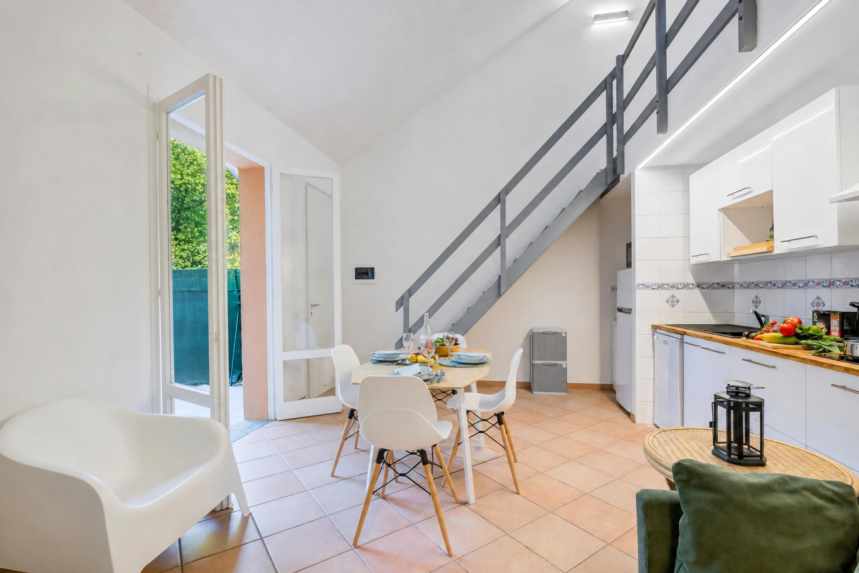 Una cocina moderna con armarios blancos, encimera de madera y una escalera que sube a un nivel superior.