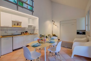 A modern kitchen with white cabinets, a dining table set with plates and glasses, and a white sofa in the living area. - France Apartment (Ispra)