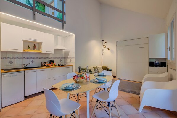 A modern kitchen with white cabinets, a dining table set with plates and glasses, and a white sofa in the living area.