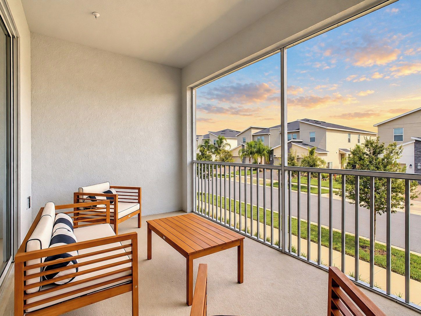 A balcony with a wooden table and chairs, a view of a residential area, and a clear sky.