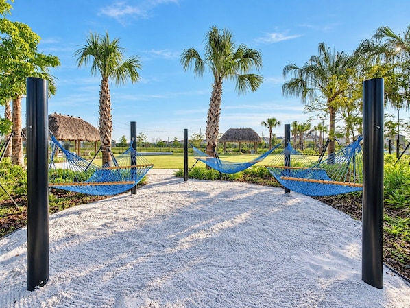 A pathway leading to a beach area with two hammocks and palm trees.