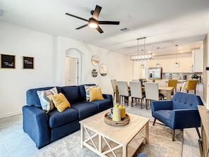 A modern living room with a blue sofa, a coffee table, and a dining area with chairs and a table.