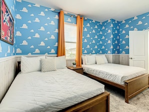 A bedroom with two beds, a window with curtains, and a wall with a cloud pattern.