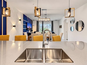 A modern kitchen with a stainless steel sink, yellow chairs, and pendant lights.