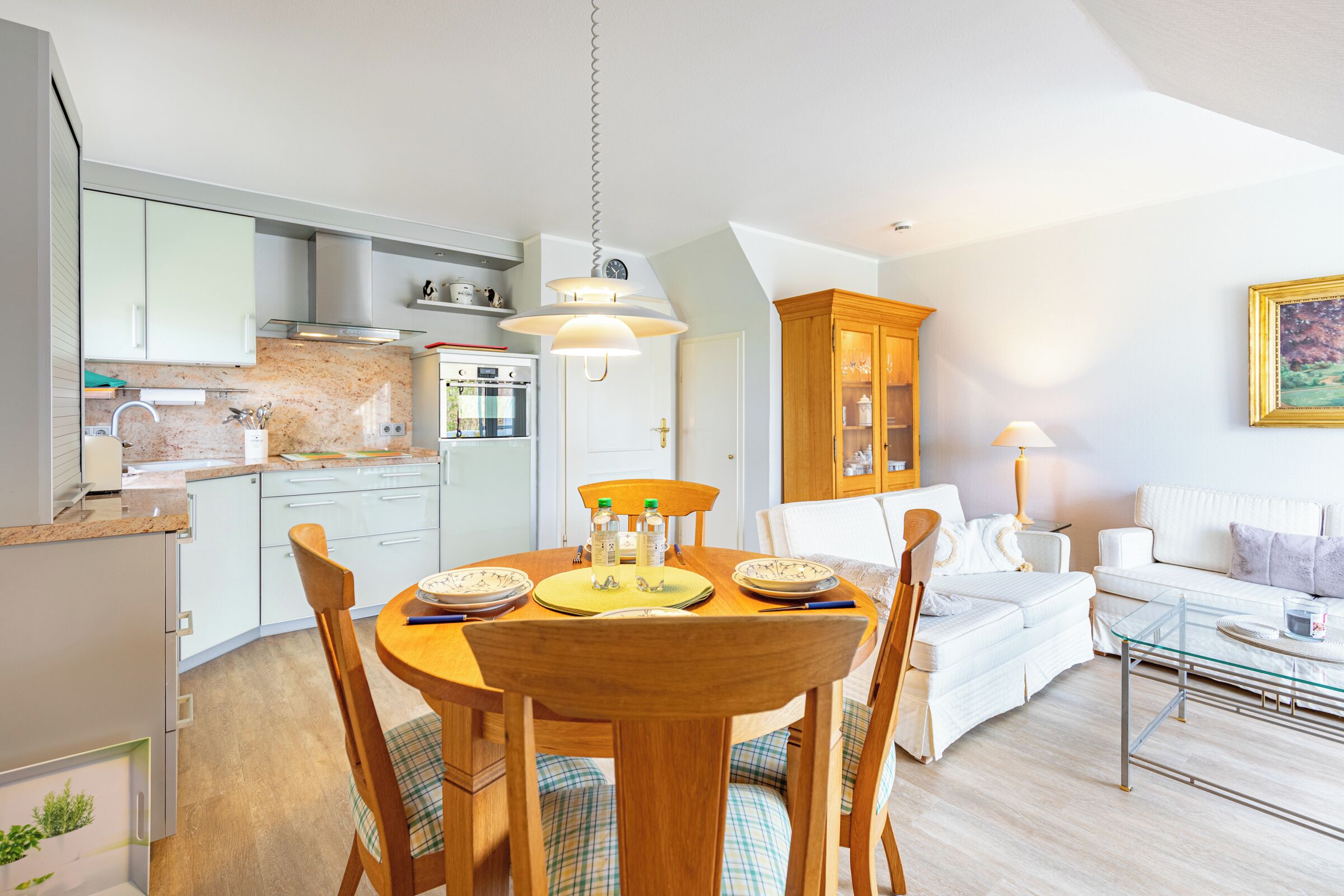 A modern kitchen with white cabinets, a dining table with chairs, and a living area with a sofa and a glass coffee table.