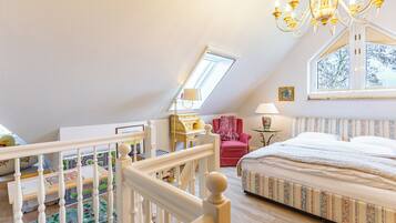A bedroom with a sloped ceiling, a bed, a window, a chandelier, and a toy train set.