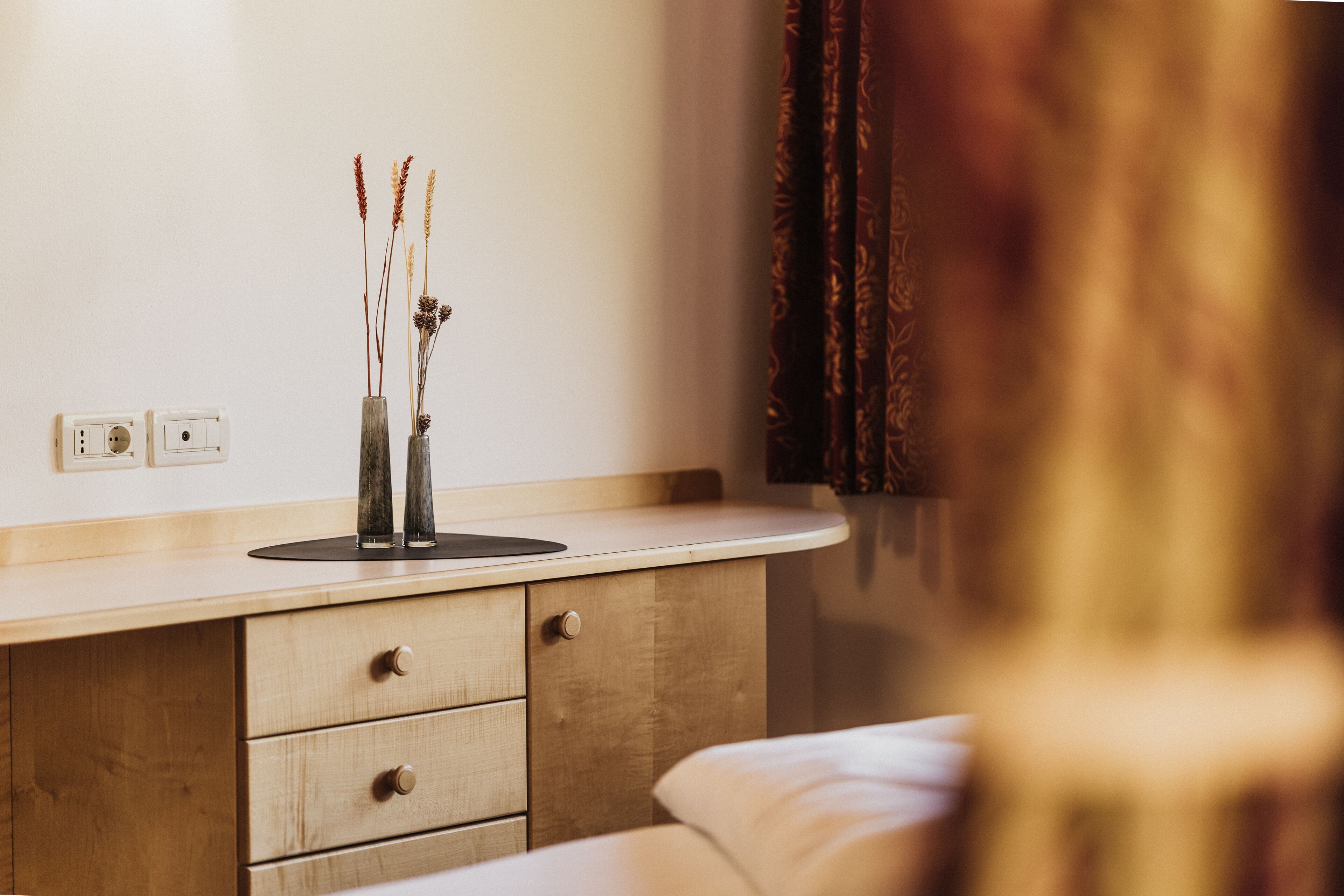 A bedroom with a wooden dresser, a bedside table, and a nightstand.