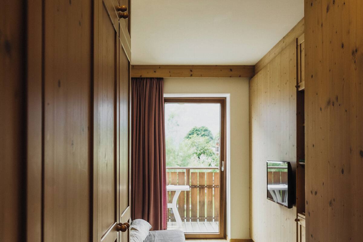 A wooden interior hallway leading to a balcony with a bed and a TV mounted on the wall.
