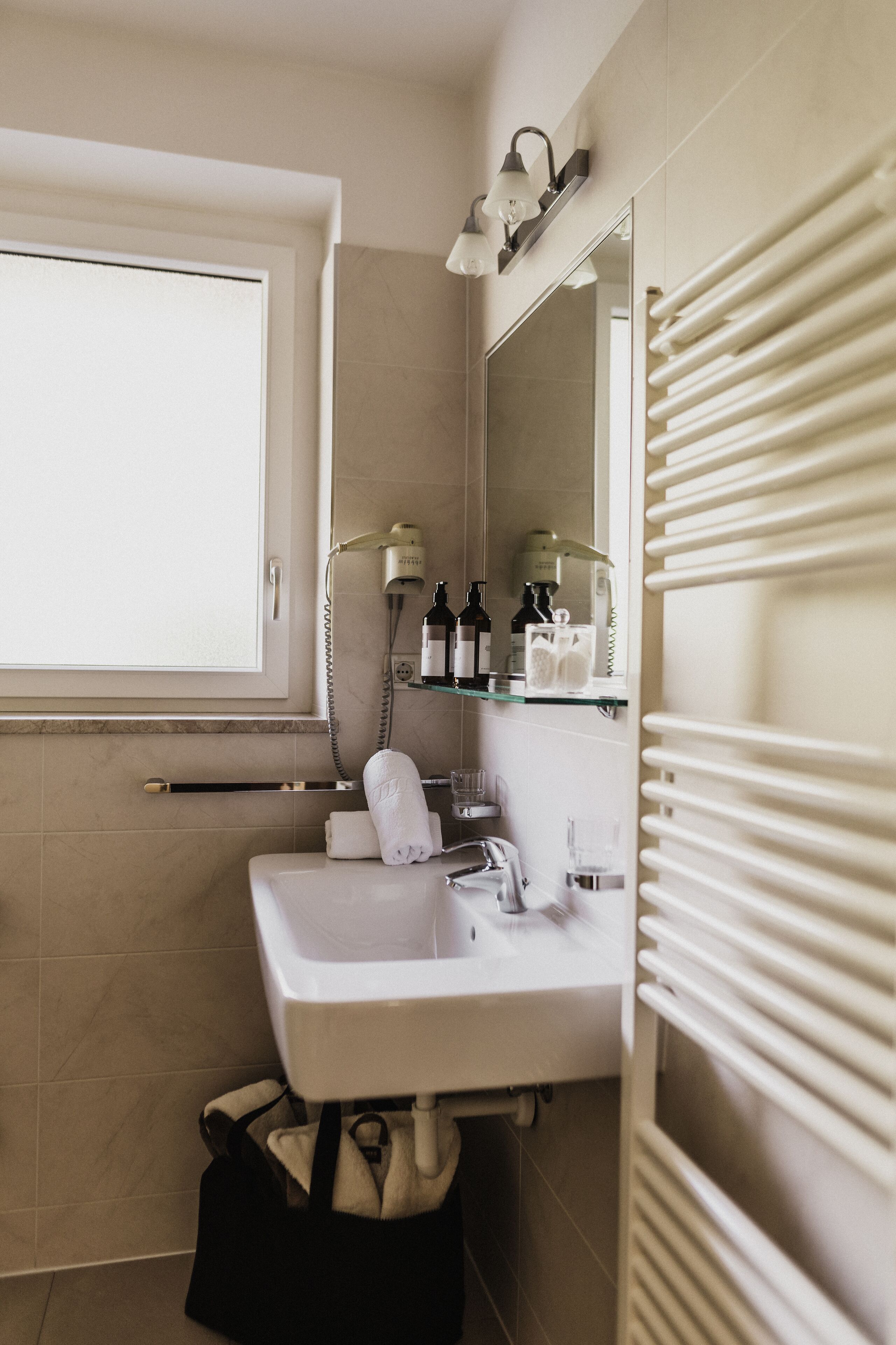 Une salle de bain équipée d’un lavabo, d’un miroir, d’un porte-serviettes et d’une fenêtre.