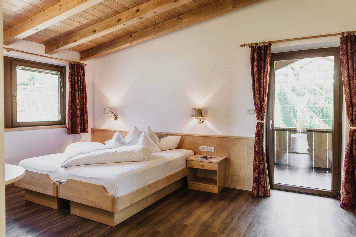 A wooden-framed room with a bed, bedside table, and a window with curtains.