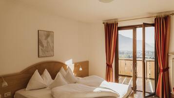 Habitación de hotel con cama, mesita de noche, lámpara, un cuadro y balcón con cortinas.