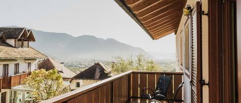 Ein Balkon mit Holzgeländern, einem Stuhl und Blick auf die Berge im Hintergrund.