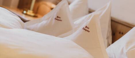 A hotel room with neatly made beds, pillows with embroidered text, a bedside lamp, and a wooden headboard.
