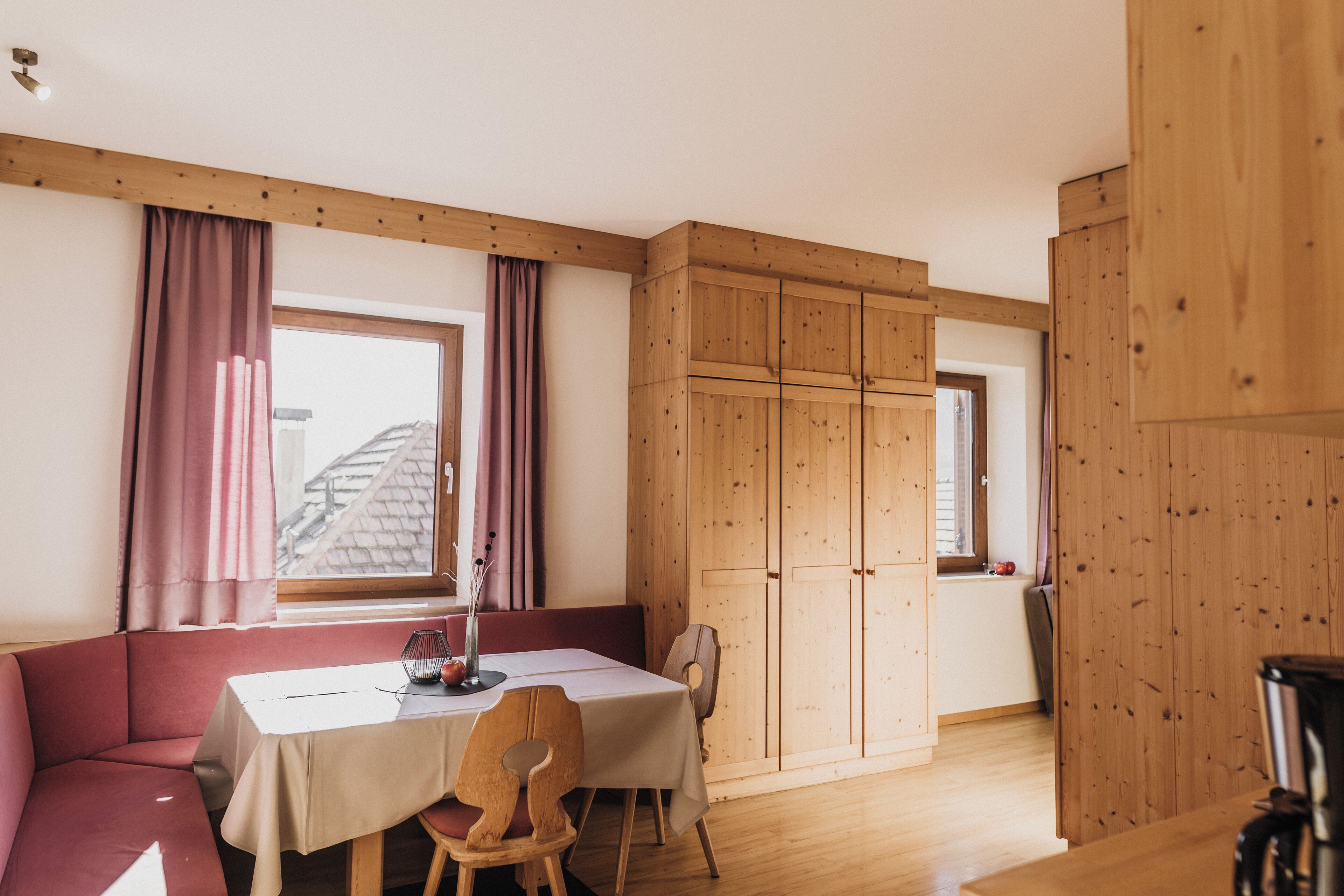 Una habitación con techo de madera, una mesa con mantel blanco, un sofá rojo y un armario de madera.
