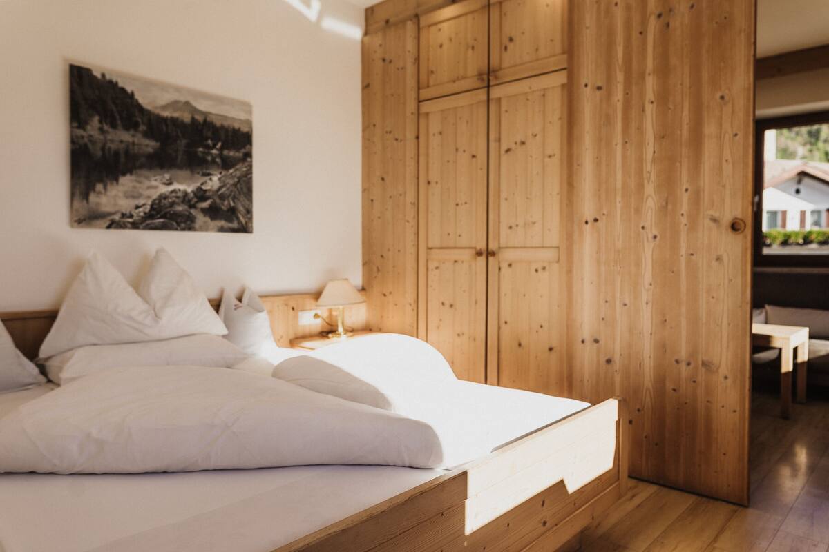 A bedroom with a wooden wardrobe, a bed with white bedding, and a painting on the wall.