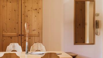 A wooden dining table with chairs, a vase with dried plants, and a mirror on the wall.