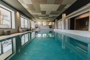 Une piscine intérieure moderne avec des murs en verre transparent, de grandes fenêtres et un plafond au design géométrique.