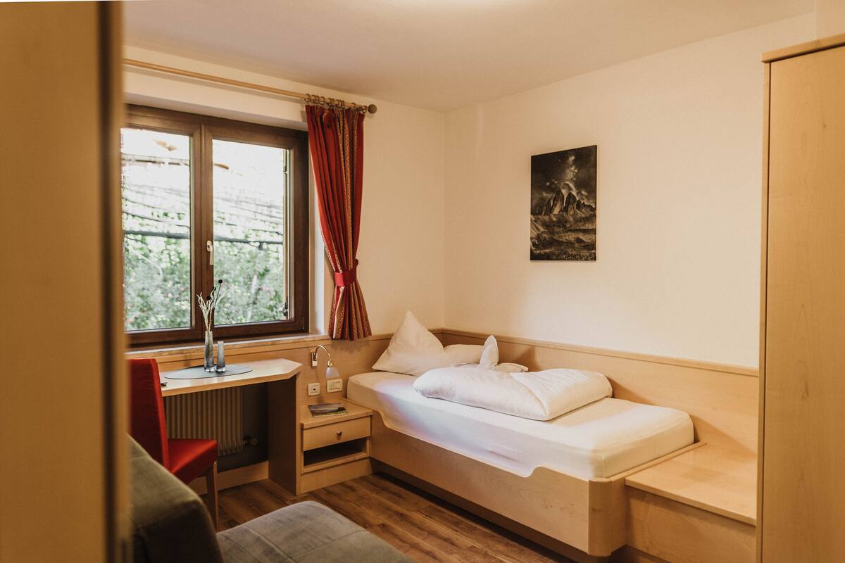 A small, cozy room with a bed, a desk, and a window with curtains.