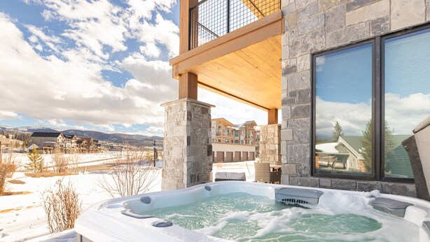 A hot tub with a view of a snowy landscape and a building with stone walls and large windows. - Luxury Condo with Private Hot Tub: Alpenglow Chalet (Fraser)