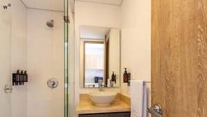A bathroom with a glass shower enclosure, a wooden vanity with a white sink, and a mirror above the sink. - w* | Charming loft in the heart of Santa Barbara (Bogotá)