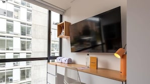 Un espace de bureau moderne doté d’une grande fenêtre, d’un bureau, d’une chaise, d’un téléviseur et d’une lampe.