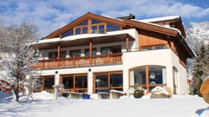 Un chalet a due piani con un balcone in legno, ampie finestre e un paesaggio innevato.