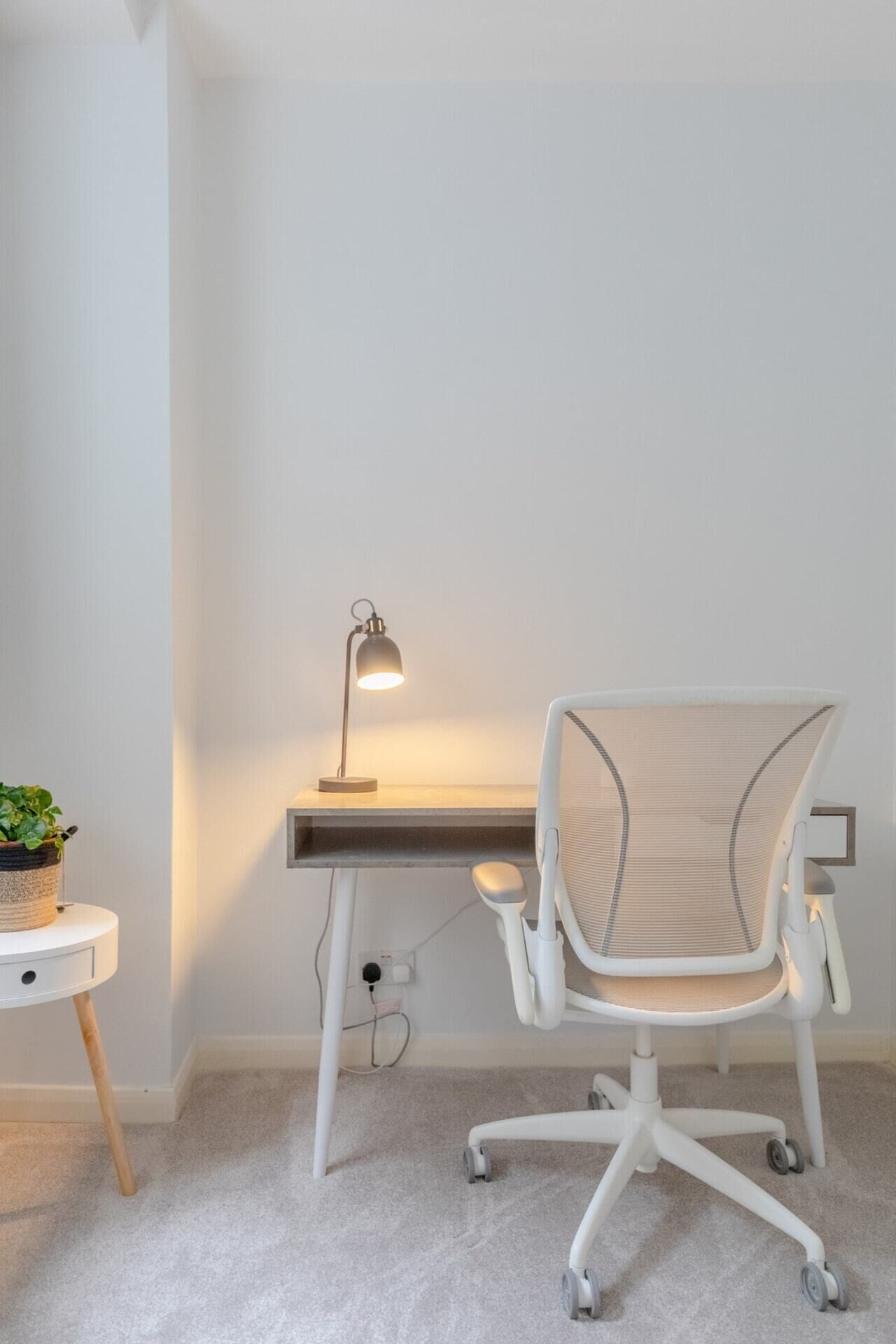 Un espace de travail comprenant un bureau, une chaise, une lampe et une petite table sur laquelle est posée une plante.