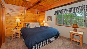 A bedroom with a wooden ceiling, a large window with a view of trees, and a bed with striped bedding. - Tree Top Villa By Destination Big Bear:Upper Moonridge! Decks! Pool/Ping Pong Table! Foosball! (Big Bear City)