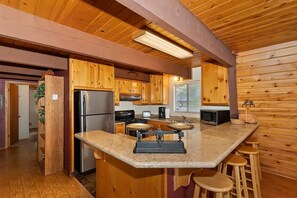 A kitchen with wooden cabinets, a granite countertop, a stainless steel refrigerator, a stove, and a microwave. - Tree Top Villa By Destination Big Bear:Upper Moonridge! Decks! Pool/Ping Pong Table! Foosball! (Big Bear City)