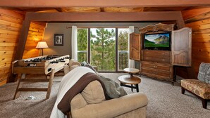 A cozy room with a sofa, a television, a foosball table, and a view of trees through a large window. - Tree Top Villa By Destination Big Bear:Upper Moonridge! Decks! Pool/Ping Pong Table! Foosball! (Big Bear City)